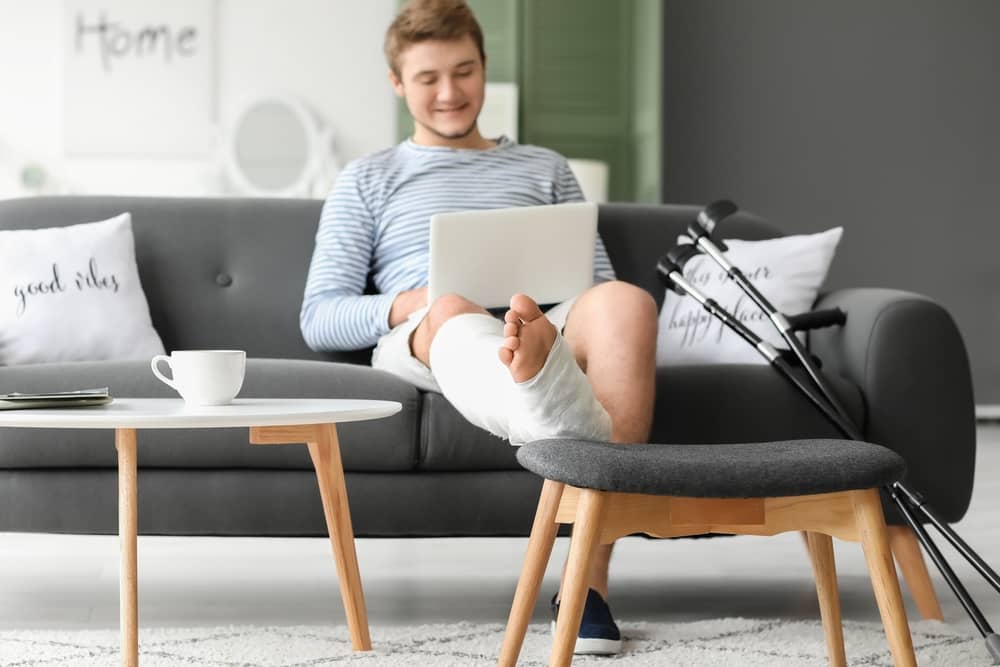 young man on couch with foot up next to crutches