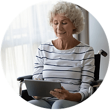 Dame aînée en chaise roulante utilisant une tablette pour lire au sujet des soins complexes virtuels.