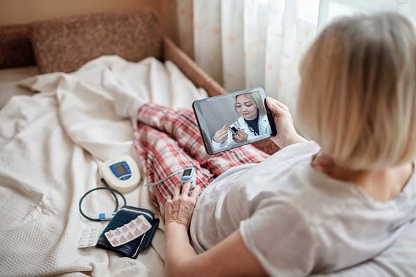 woman in bed taking blood pressure on video call
