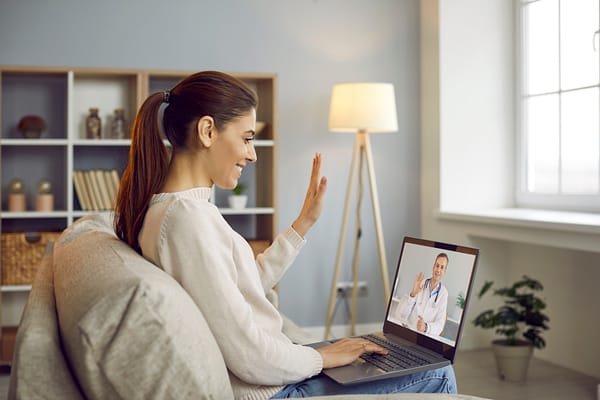 Woman smiling and waving at doctor on computer